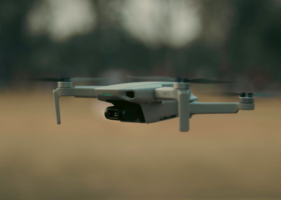 Small black drone flying in sunny park with trees